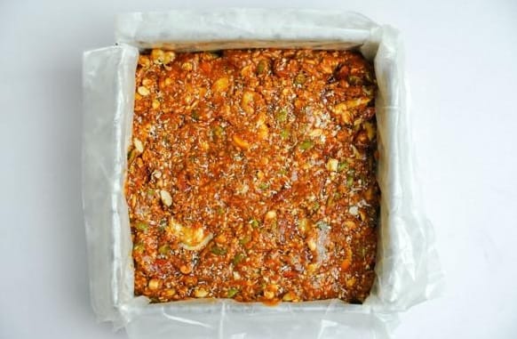Protein bar mixture pressed firmly into a parchment-lined pan and topped with crushed pistachios