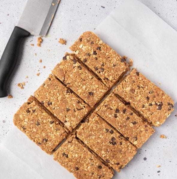 Chilled protein bar slab sliced into even bars on parchment paper, with a knife alongside