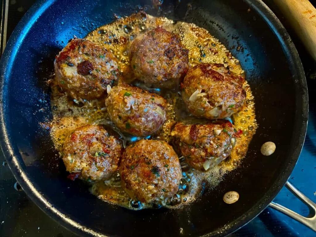 Meatballs searing in a skillet, developing a deep brown crust
